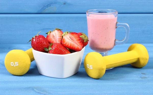 Fresh ripe strawberries, delicious milkshake and dumbbells, concept of healthy and sporty lifestyle — Stock Photo, Image