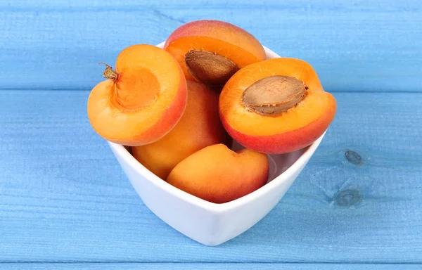 Aprikot matang segar dalam mangkuk kaca di papan biru, konsep makanan penutup yang sehat — Stok Foto