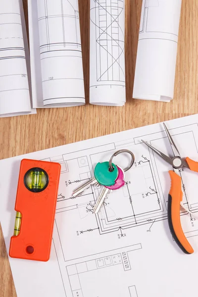 Home keys with electrical drawings or blueprints and orange work tools, concept of building home