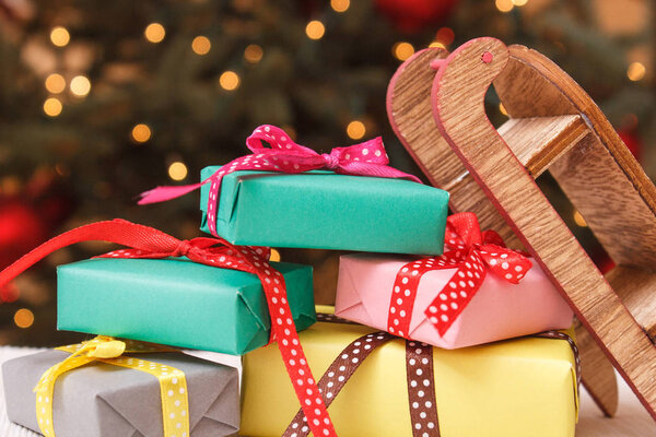 Красочные завернутые подарки с деревянными санями и рождественская елка с огнями на заднем плане, праздничная концепция времени
