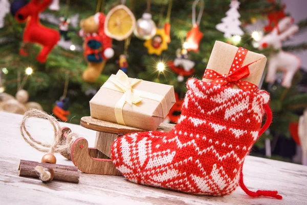 Radbruten julklapp med band på släde och i strumpan på bakgrund av julgran med dekoration — Stockfoto
