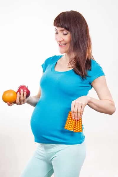 Zwangere vrouw met vers fruit en medische pillen of supplementen, keuze tussen gezond voedsel en tabletten — Stockfoto