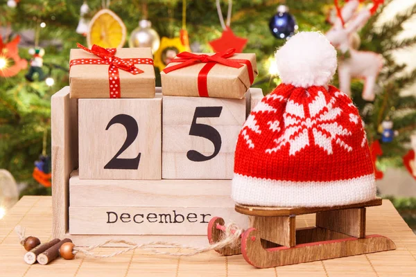 Datum 25 December på kalender, gåvor med släde och cap, julgran med dekoration, festlig tid koncept — Stockfoto