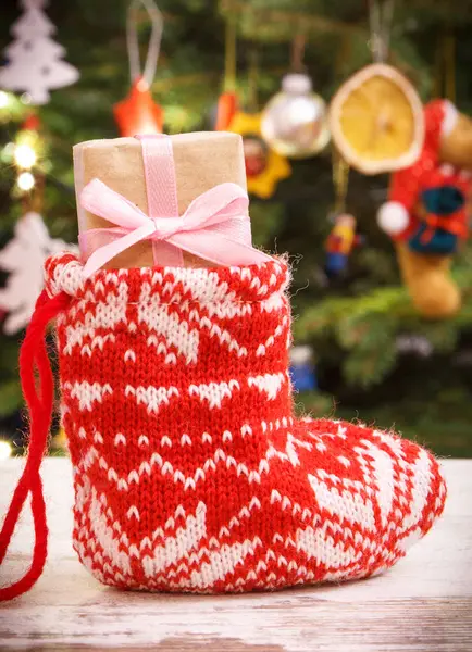 Radbruten julklapp med band i röd strumpa på bakgrund av julgran med dekoration — Stockfoto