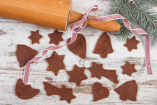 Rolling pin, dough for Christmas cookies in various shapes and spruce branches on old rustic board — Stock Photo, Image