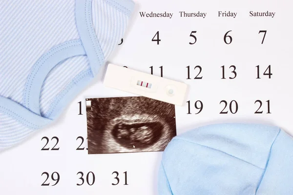 Pregnancy test, ultrasound scan of baby and clothing for newborn on calendar, concept of extending family