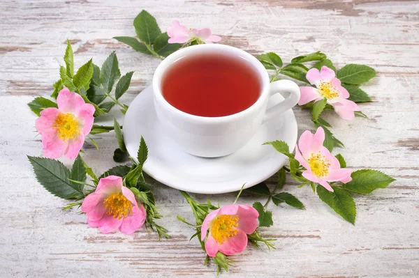 Tasse Tee und Wildrosenblume auf altem rustikalen Brett — Stockfoto