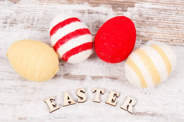 Inscription Easter and colorful eggs wrapped woolen string on rustic board — Stock Photo, Image