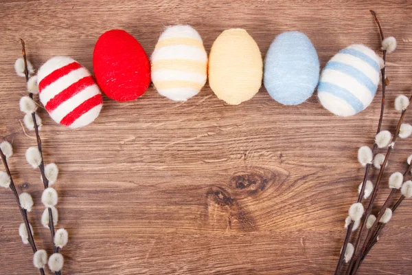 Twigs of willow and colorful Easter eggs wrapped woolen string on rustic board, copy space for text — Stock Photo, Image