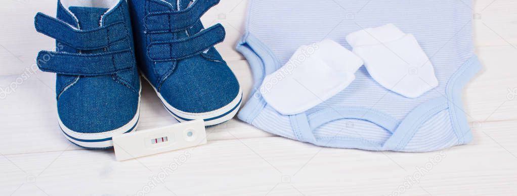 Pregnancy test with positive result and clothing for newborn baby, expecting for baby