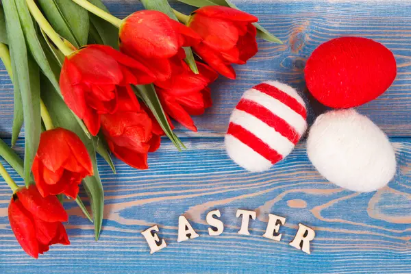 Wielkanoc napis, czerwone tulipany i jaja pakowane wełniane ciąg na deski, Świąteczna Dekoracja — Zdjęcie stockowe