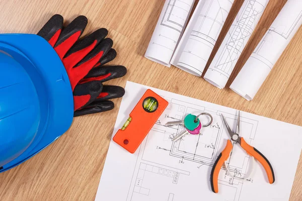 Home keys with electrical drawings, protective helmet with gloves and orange work tools, concept of building home
