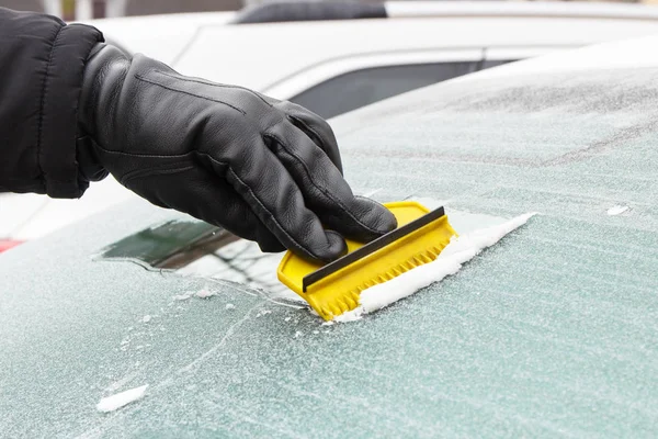 Mão em luva de couro raspando gelo ou neve da janela do carro — Fotografia de Stock