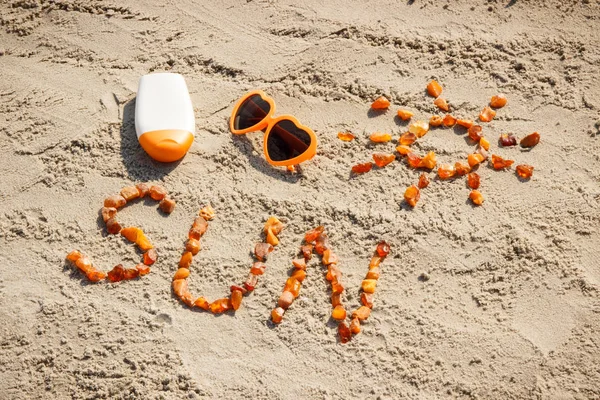 Word and shape of sun, sunglasses with sun lotion on sand at beach, summer time concept — Stock Photo, Image