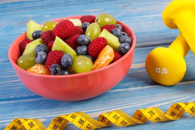 Taze meyve salatası ve halter, sağlıklı yaşam ve beslenme kavramı ile şerit metre