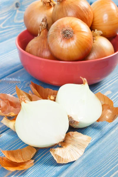 Geschälte und ungeschälte frische Zwiebeln auf blauen Brettern, gesundes Ernährungskonzept — Stockfoto