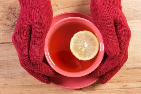 Mano de mujer en guantes sosteniendo taza de té caliente en la mesa — Foto de Stock