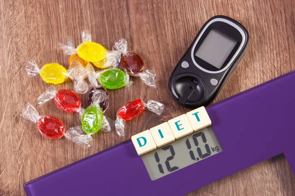 Electronic bathroom scale, glucometer with result of measurement and colorful candies, diabetes and reduction eating sweets concept