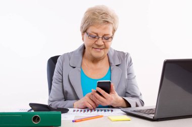 Smartphone kullanarak ve ofis masasında çalışan yaşlı bir iş kadını