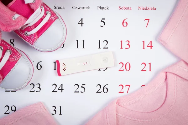 Test di gravidanza con risultato positivo e abbigliamento per neonato sul calendario — Foto Stock