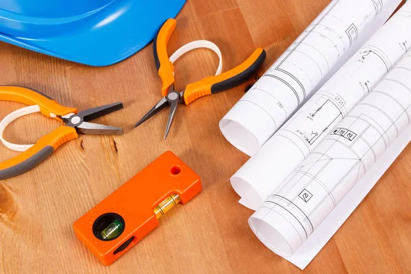 Электрические чертежи, защитный синий шлем и оранжевые инструменты для инженерных работ, лежащих на столе — стоковое фото