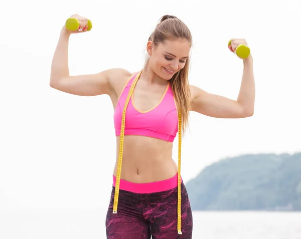 Chica delgada en ropa deportiva con centímetro haciendo ejercicio con pesas en la playa —  Fotos de Stock