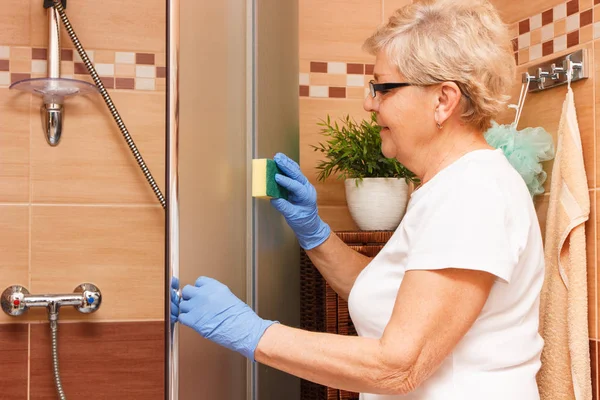 Пожилая женщина вытирает стекло для душа, уборка дома и обязанности по дому — стоковое фото