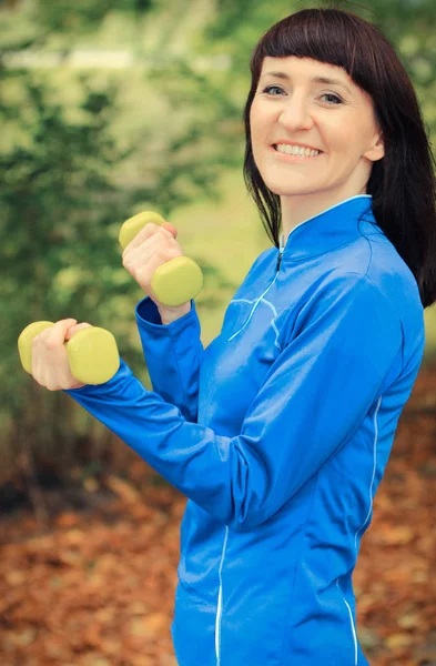 Leende kvinna i sportiga kläder tränar med hantlar i park — Stockfoto