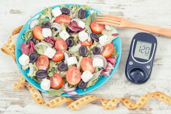 Glucose meter and fresh greek salad with feta cheese and vegetables. Best food for diabetics, dieting and slimming
