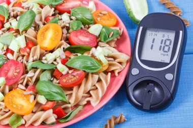 Şeker seviyesini ölçmek için glikoz ölçer ve kepekli makarna ve sebzelerle taze salata. Şeker hastaları için en iyi yemek.