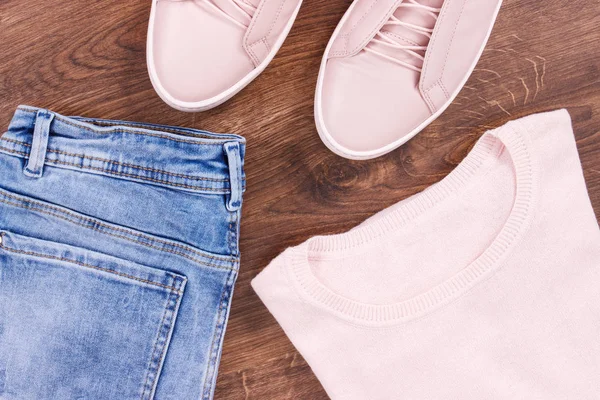 Жіноче рожеве шкіряне взуття, джинсові штани та светр на сільських дошках — стокове фото