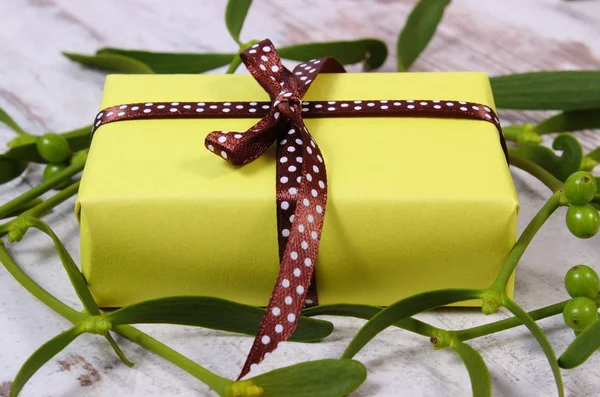 Wrapped yellow gift for Christmas and mistletoe on old wooden background — Stock Photo, Image