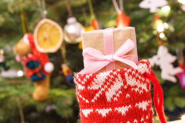 Τυλιγμένο δώρο με κορδέλα για τα Χριστούγεννα στην κόκκινη κάλτσα σε φόντο χριστουγεννιάτικο δέντρο διακόσμηση — Φωτογραφία Αρχείου