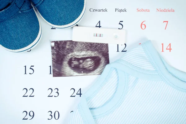 Test di gravidanza, ecografia del bambino e abbigliamento per neonato sul calendario con parole lucide, in attesa per il bambino — Foto Stock