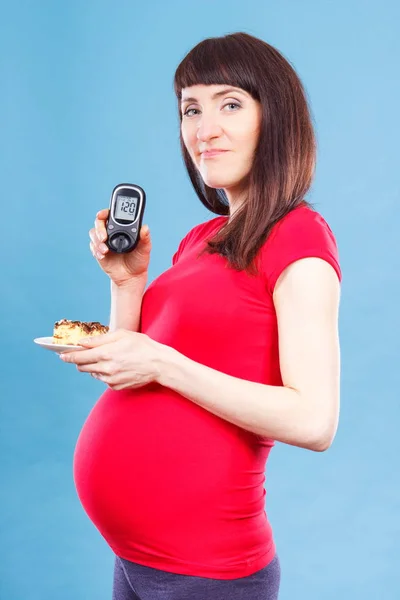 Беременная женщина держит глюкометр с результатом уровень сахара и кусок чизкейка, диабет и питание во время беременности — стоковое фото