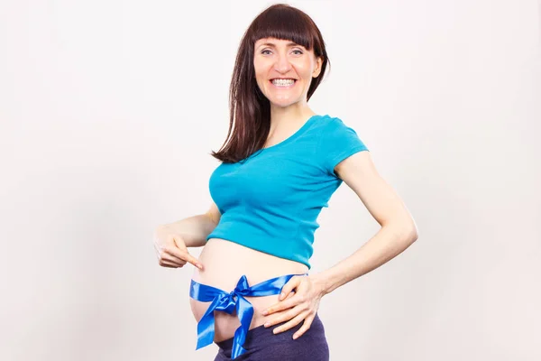 Feliz mujer embarazada sonriente mostrando su vientre con cinta azul, concepto de espera para el niño recién nacido — Foto de Stock