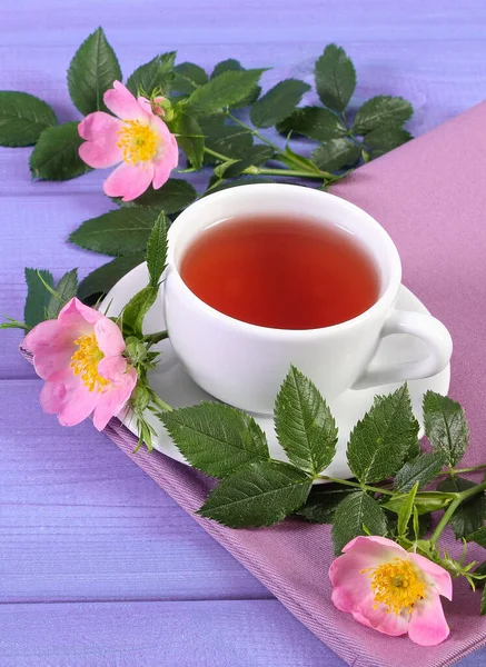 Xícara de chá e flor de rosa selvagem em placas roxas — Fotografia de Stock