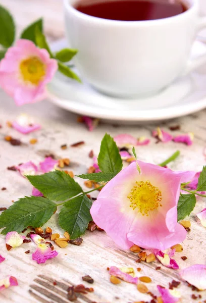 Wildrosenblume und Tasse Tee auf altem rustikalem Holzgrund — Stockfoto