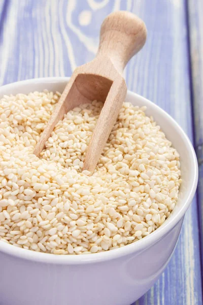 Sesame seeds with wooden scoop in white bowl on boards — Stock Photo, Image