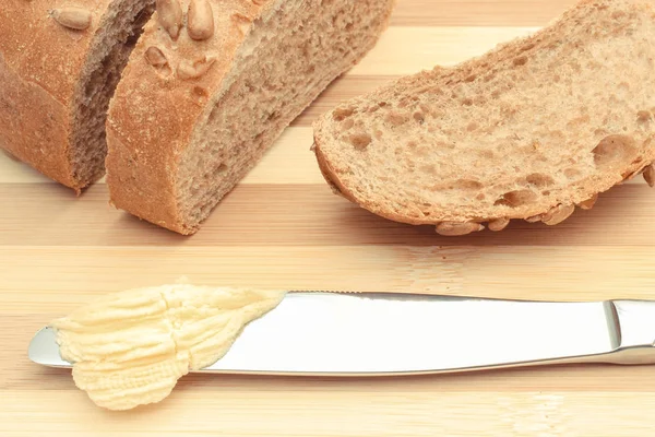 Mantequilla en el cuchillo y rebanada de pan en la tabla de cortar — Foto de Stock