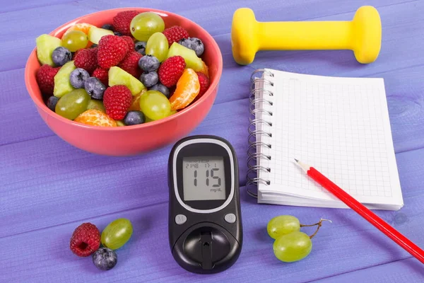 Fresh fruit salad, glucose meter with result of sugar level and notepad for writing notes or resolutions, concept of diabetes, diet, slimming, healthy lifestyles and nutrition