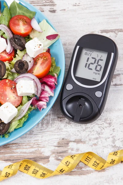 Glucometer with result of sugar level and fresh greek salad with feta cheese and vegetables. Best healthy food for diabetics, dieting and slimming