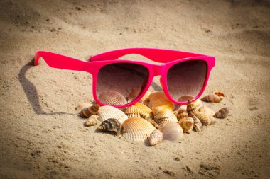 Deniz kabuğu yığını ve kumsalda uzanan pembe güneş gözlüğü, tatil ve yaz zamanı, göz koruma.