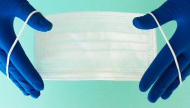 Bir çift ince mavi lateks eldiven ve beyaz arka planda yüz kalkanı. Tek kullanımlık lastik eldiven ve maske. Koruyucu denekler. İlaçlar..