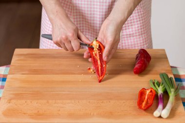 Ahşap bir tahtada kırmızı biber soyarken ve keserken ellerinizi kapatın. Sağlıklı gıda hazırlama konsepti