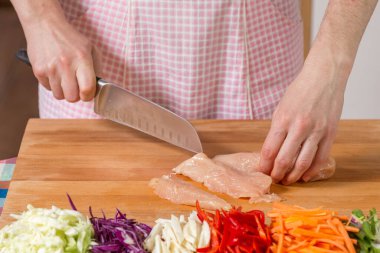 Tahta bir tahtanın üzerinde tavuk göğsünü kesen elleri kapatın. Sağlıklı gıda hazırlama konsepti