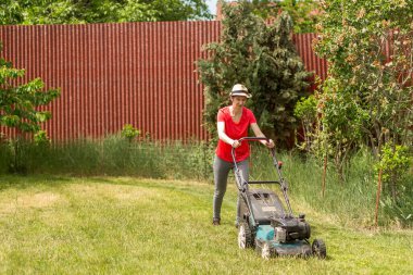 Güneşli bir günde arka bahçesinde çim biçme makinesiyle çim biçen bir kadın..