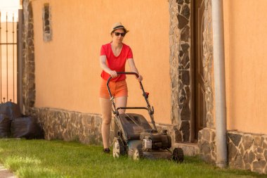 Güneşli bir günde arka bahçesinde çim biçme makinesiyle çim biçen bir kadın..