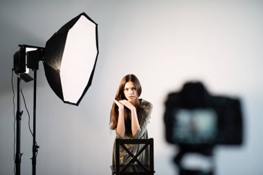 Bir kız kameranın önünde poz veriyor, üzerinde bir fener duruyor, bir kamera tripodun üzerinde kızın önünde duruyor.,