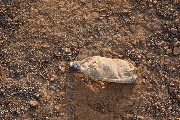 an old plastic bottle lies on the ground, yellow sand and stones on lifeless earth, a crumpled bottle thrown by people, environmental pollution, garbage in nature,